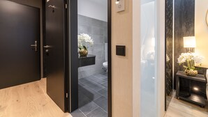A modern bathroom with a dark door, a toilet, and a sink. There is a small shelf with a vase of flowers. - PLAZA INN Wiener Neustadt, BW Signature Collection (Wiener Neustadt)