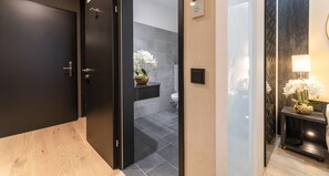 A modern bathroom with a dark door, a toilet, and a sink. There is a small shelf with a vase of flowers. - PLAZA INN Wiener Neustadt, BW Signature Collection (Wiener Neustadt)