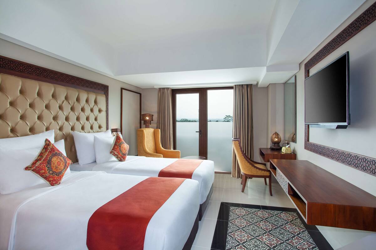 Une chambre d’hôtel avec deux lits, un bureau, une chaise, une télévision et une vue sur l’extérieur.