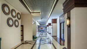 A hallway with a patterned floor, decorative wall clocks, and a geometric ceiling design. - Alhambra Hotel & Convention, Bw Signature Collection (Singaparna)