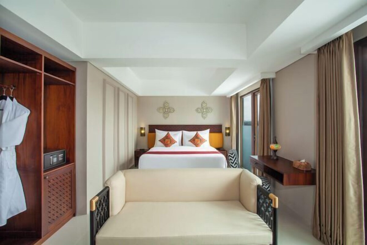 A hotel room with a bed, a bedside table with a lamp, a wardrobe, and a large window with curtains.