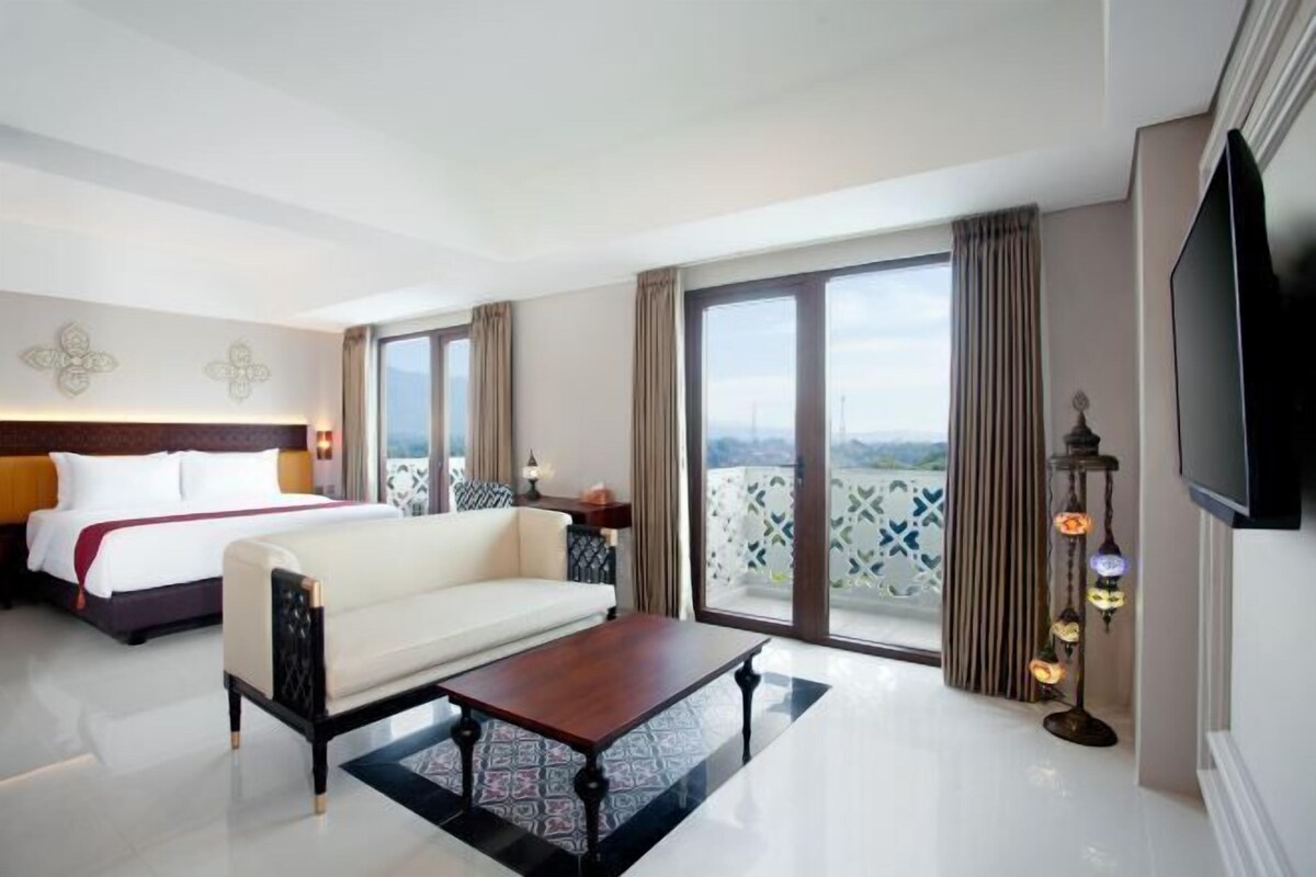 A hotel room with a bed, a sofa, a coffee table, a TV, and a balcony with a view.