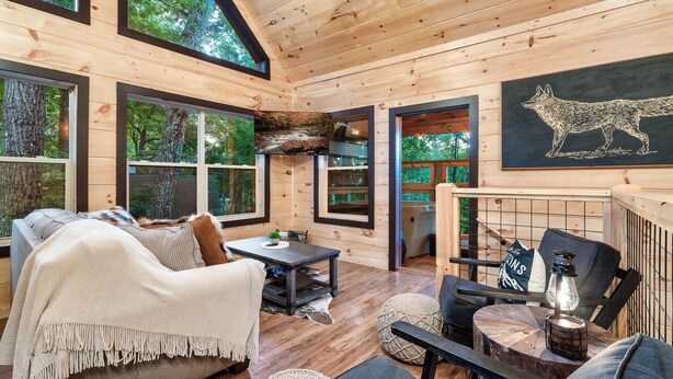 Ein gemütliches Blockhaus-Interieur mit Holzboden, großen Fenstern, einem Kamin und einem Essbereich.