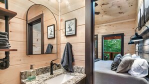 Ein Holzblockhaus Innenansicht mit einem Badezimmer, das ein Waschbecken mit Granitplatte, einen Spiegel und einen Handtuchhalter beinhaltet.