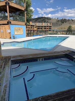 A swimming pool with a tiled deck and a wooden deck area. There are lounge chairs and a lifeguard chair.