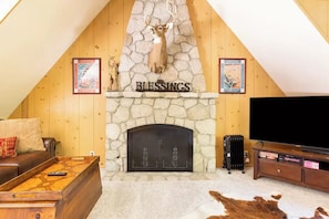 Una sala de estar acogedora con una chimenea de piedra con la leyenda "BLESSEMS", un sofá de cuero, una mesa de centro, un televisor y un radiador.