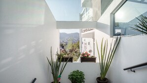 Un balcón con plantas en macetas, techo de cristal y vista a un paisaje urbano.