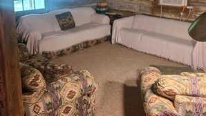 Interior de una cabaña de troncos con dos sofás, una mesita y un ventanal con persianas.