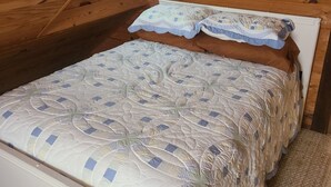 Techo de madera con diseño inclinado, cama con colcha estampada y cabecero de madera.