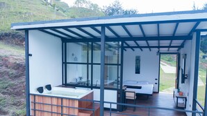 A modern cabin with a wooden deck, a large window, and a bedroom with a bed and a desk.