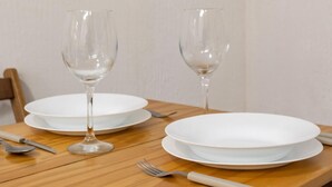 Una mesa de comedor con dos platos blancos, dos copas de vino, un tenedor y un cuchillo.