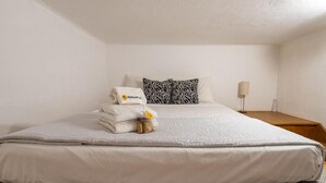 Una cama bien hecha con un edredón blanco, dos almohadas con estampado de cebra y una toalla doblada con el logotipo de una piña.