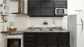 Una cocina con armarios negros, estufa blanca, microondas y pileta.