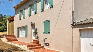 Un bâtiment à deux étages, doté d’une façade beige, de volets verts et d’un porche dont le toit est recouvert de tuiles rouges.