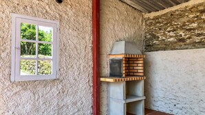 Une pièce rustique avec un mur à la texture particulière, une fenêtre donnant sur un paysage verdoyant et un four en briques apparentes.