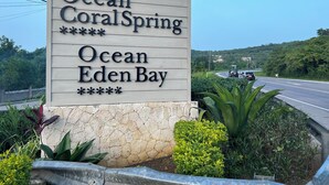 Señal de Ocean Coral Spring y Ocean Eden Bay, rodeada de vegetación y una carretera con vehículos.