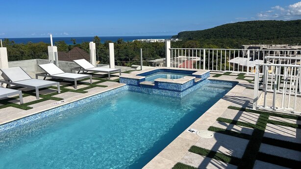 Una piscina en la azotea con agua azul cristalina, sillones de descanso blancos y vista al océano.