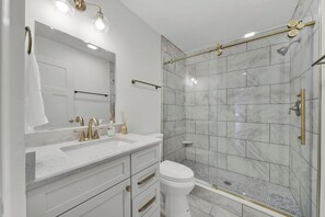 A modern bathroom with a glass-enclosed shower, white marble tiles, and gold fixtures.