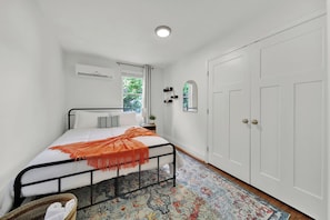 A bedroom with a bed, a window, an air conditioning unit, a wardrobe, and a patterned rug.