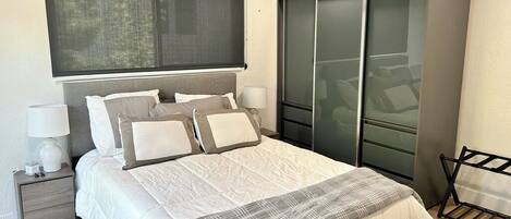 A modern bedroom with a large bed, a nightstand, a dresser, and a closet.