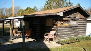 A rustic cabin with a covered porch, a small attached shed, and a single chair outside.