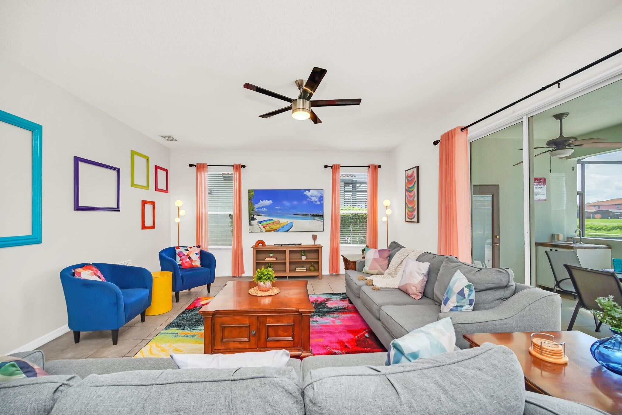 A modern living room with a ceiling fan, large windows with curtains, and a view of the outdoors.