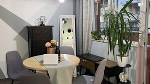 A dining area with a round table, chairs, a small cabinet, a hanging light fixture, and a potted plant.