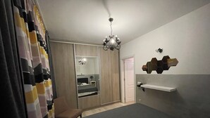 A bedroom with a bed, a chair, a wardrobe, a mirror, and a chandelier.