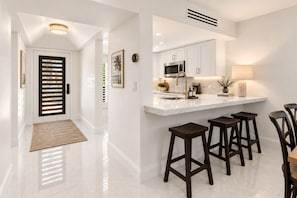 A modern kitchen with white cabinetry, a stainless steel microwave, and a bar area with stools.