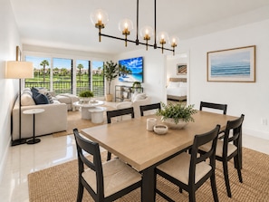 A modern living room with a dining area, large windows, and a view of a golf course.