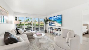 Una sala de estar moderna con un sofá color beige, una mesa de centro blanca y un cuadro con una escena de playa.