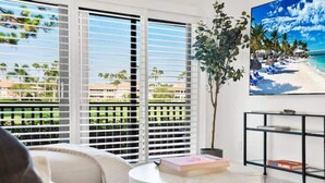 Una sala de estar con vista a la playa, una mesa redonda de centro con libros y un mueble negro para televisor.