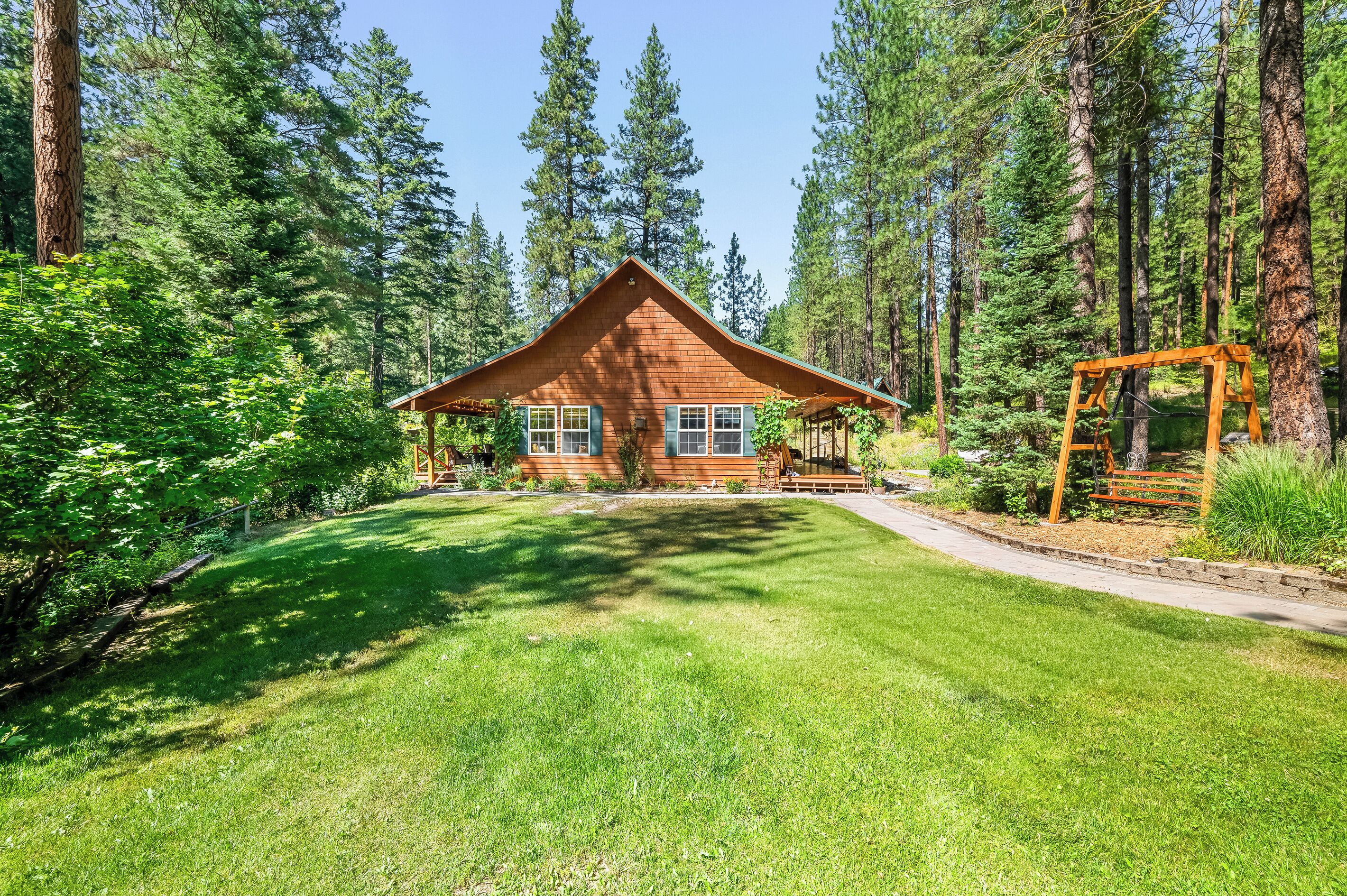 A cabin with a sloped roof, surrounded by a well-maintained lawn and tall trees.
