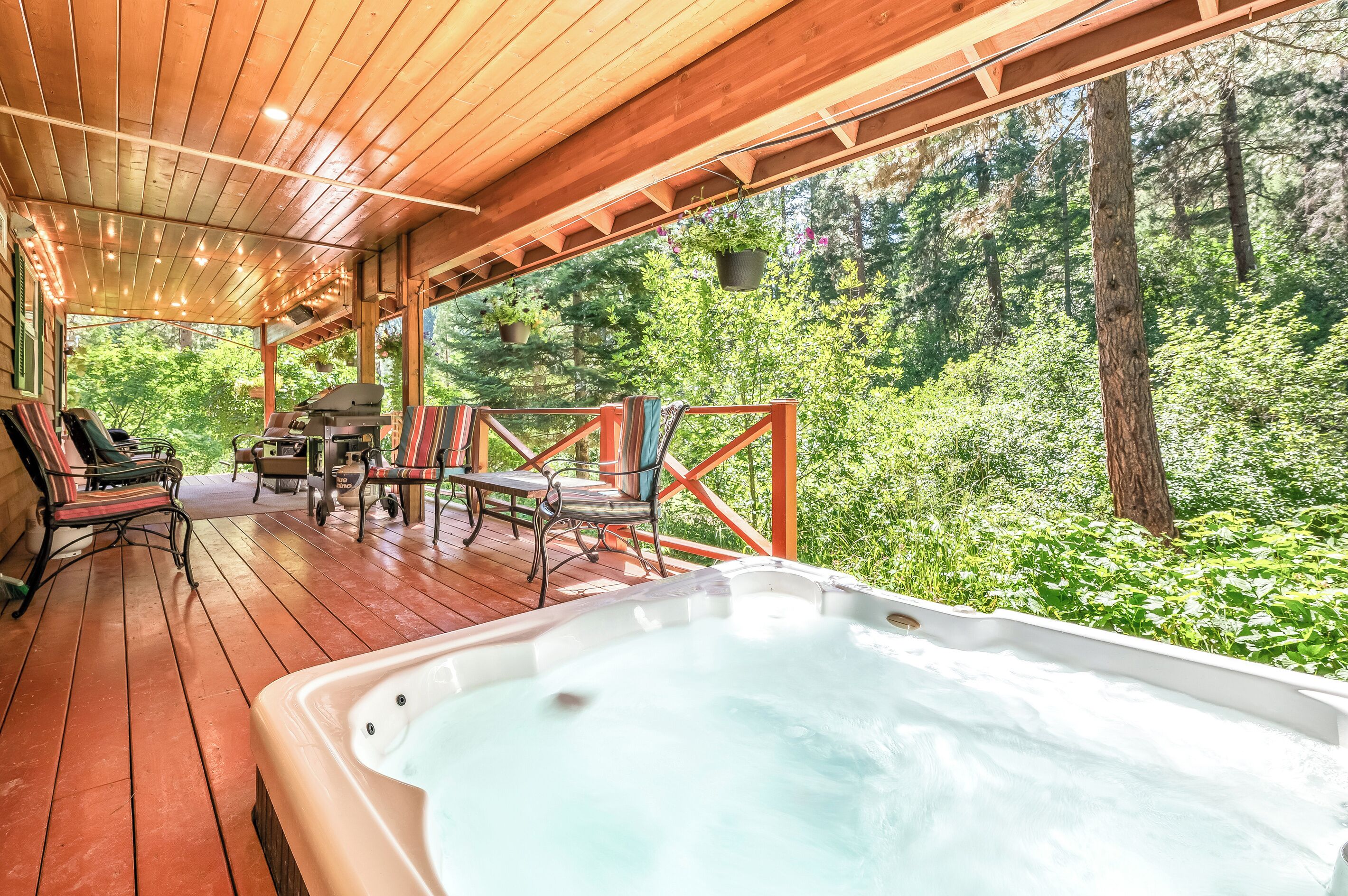 A wooden deck with a hot tub, outdoor seating, and a view of a forest.