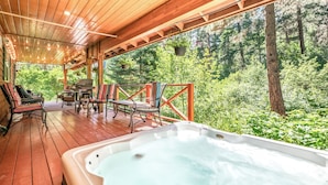 Een houten terras met een jacuzzi, buitenmeubels en uitzicht op een bos.