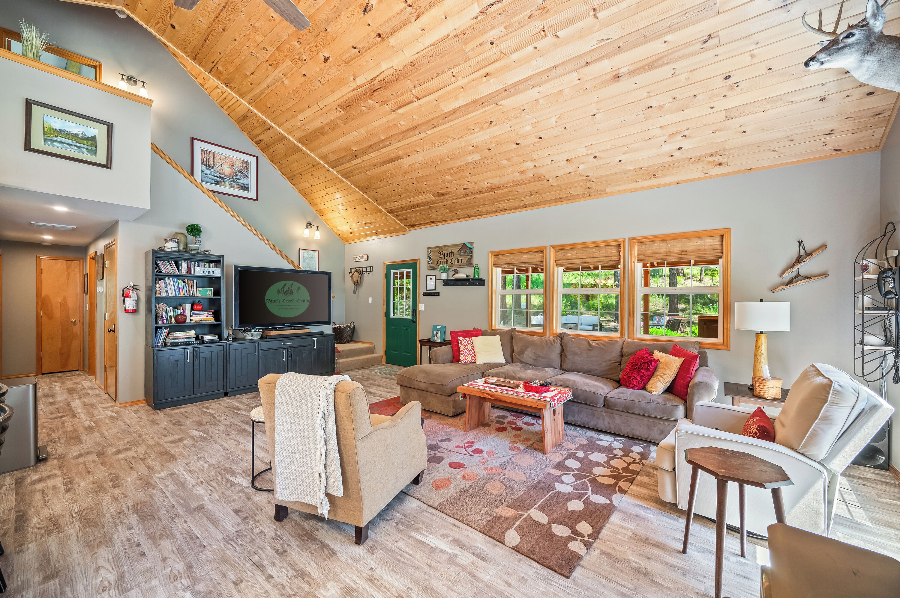 A spacious living area with a high wooden ceiling, a television, a bookshelf, and a fireplace.