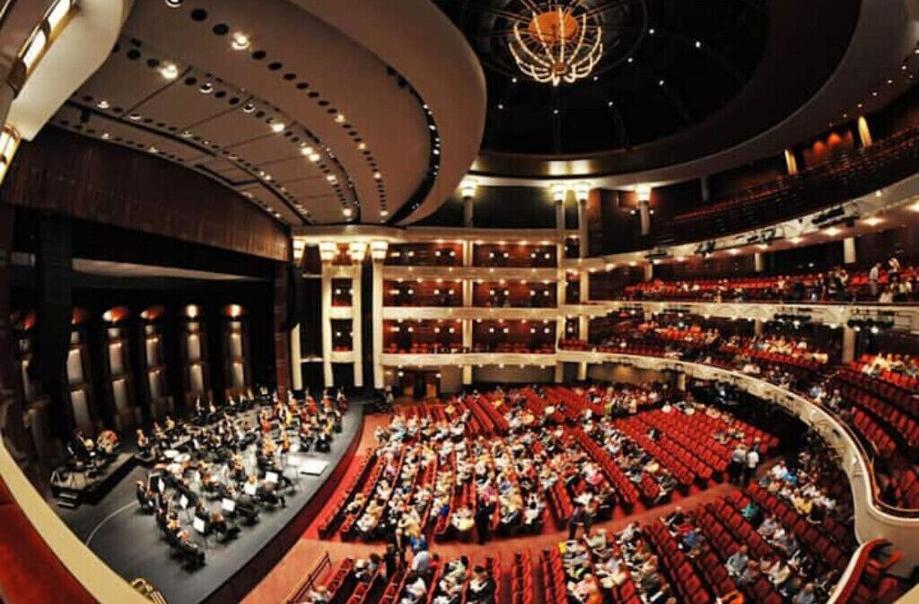 A large auditorium with tiered seating, a stage, and a grand chandelier.