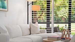 Un salon moderne avec un canapé blanc, une petite table d’appoint ronde en bois et une bibliothèque remplie de livres.