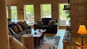 A spacious living room with a high ceiling and large windows, a stone fireplace, and a cozy seating area. - Beautiful NEW 5 br 4 bath Log cabin with PRIVATE HOT TUB overlooking Lake Lure (Lake Lure)