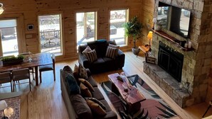 A spacious loft-style room with high ceilings, large windows, a stone fireplace, and a cozy seating area. - Beautiful NEW 5 br 4 bath Log cabin with PRIVATE HOT TUB overlooking Lake Lure (Lake Lure)