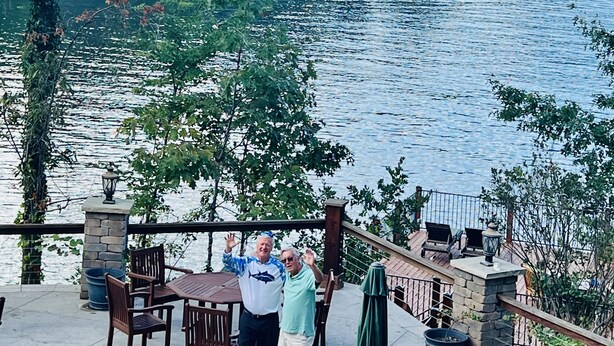 A lakeside patio with wooden tables and chairs, overlooking a calm lake and forested mountains. - Beautiful NEW 5 br 4 bath Log cabin with PRIVATE HOT TUB overlooking Lake Lure (Lake Lure)