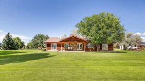 A log cabin with a large front porch, a well-maintained lawn, and a tree in front.