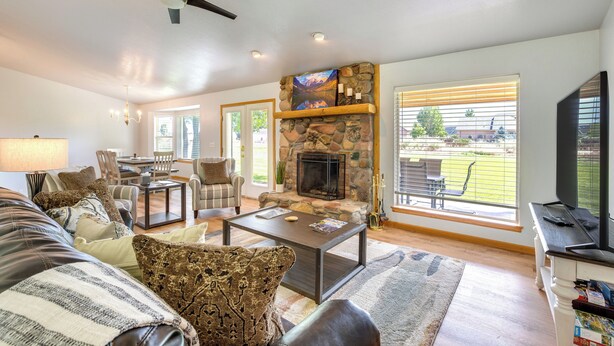 A living room with a stone fireplace, a ceiling fan, and a view of the outdoors.