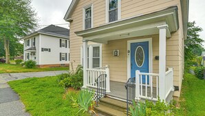 Uma casa de dois andares com varanda da frente, uma porta azul e um pequeno jardim.