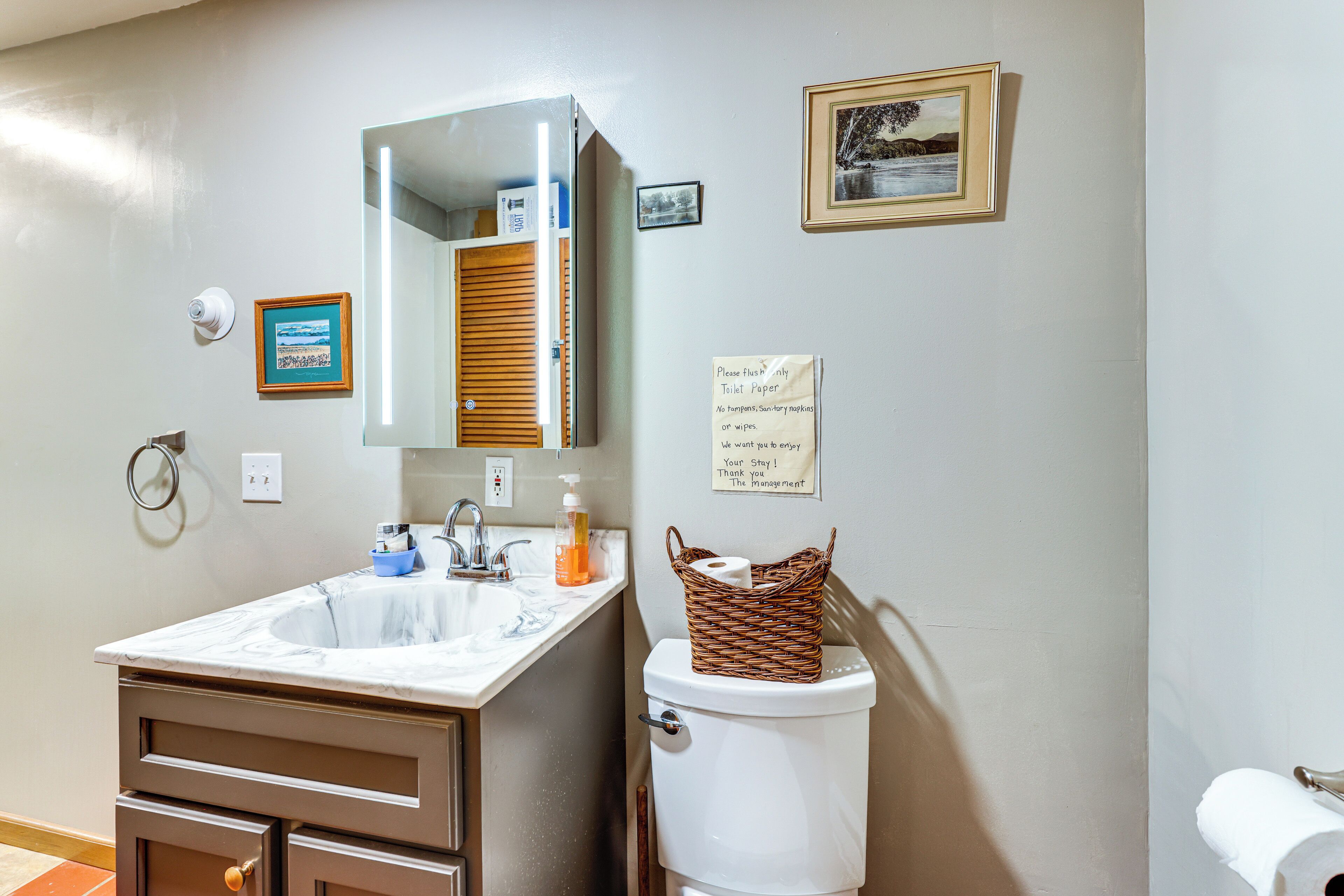 Een badkamer met een wastafel, spiegel, toilet en een mand toiletpapier aan de muur.