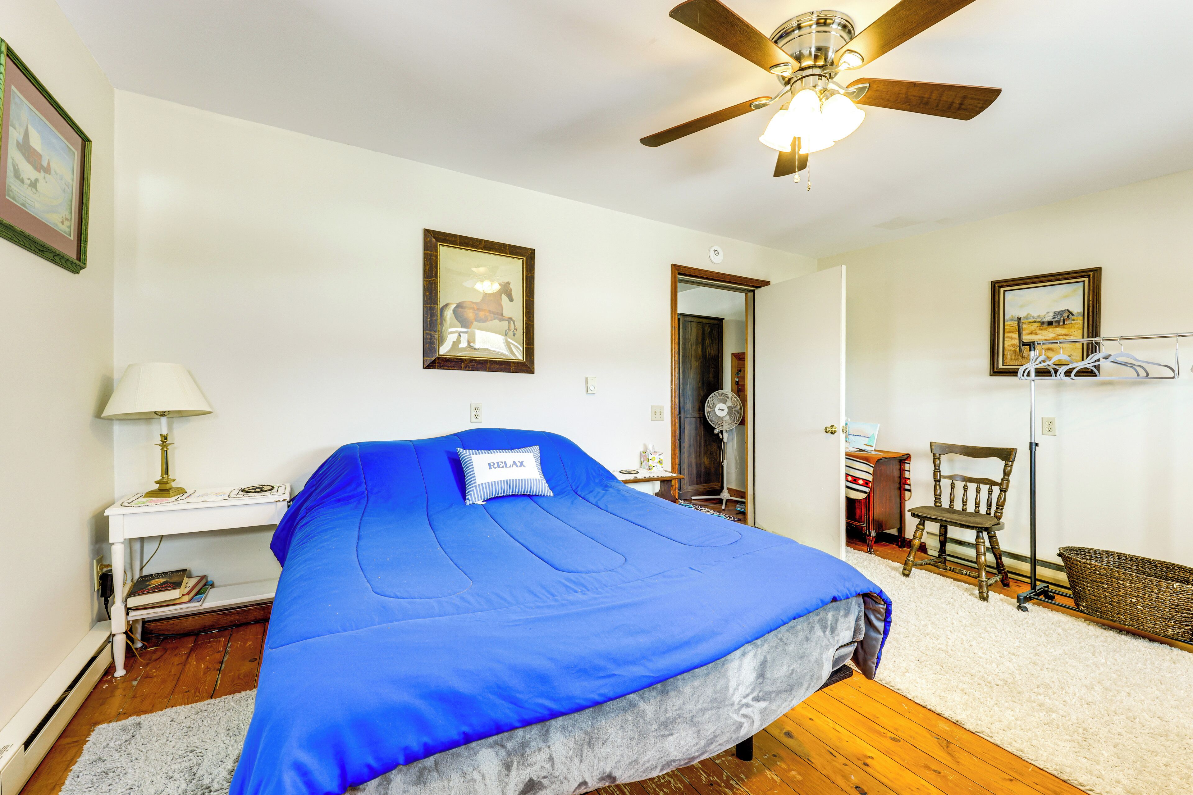 A bedroom with a bed, a desk, a chair, a ceiling fan, and a door leading to another room.