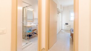 Un couloir menant à une salle de bain équipée d’une douche à parois de verre, d’un lavabo et d’un miroir.