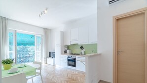 Une cuisine moderne avec des meubles blancs, un four à micro-ondes et une cuisinière. On y trouve un coin repas avec une table et des chaises, et une vue sur un balcon.