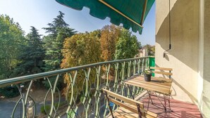 Un balcon avec une table et des chaises en bois, un auvent vert et une vue sur des arbres et une route.
