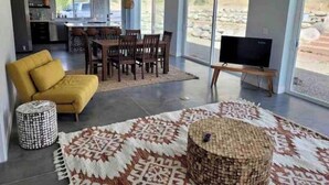 A modern living room with a sofa, dining table, chairs, a TV, and a patterned rug.